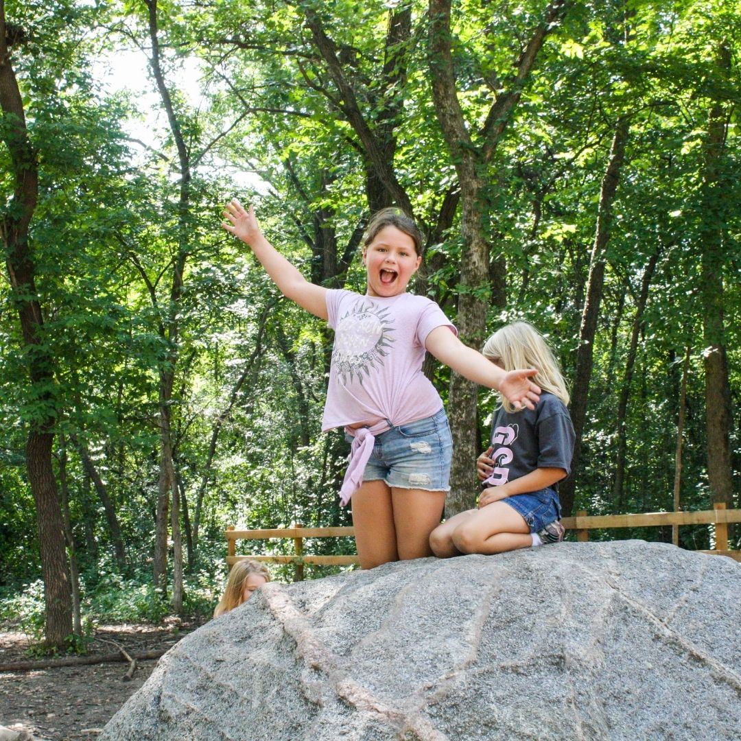 Young girl smiling on a large rock at the park