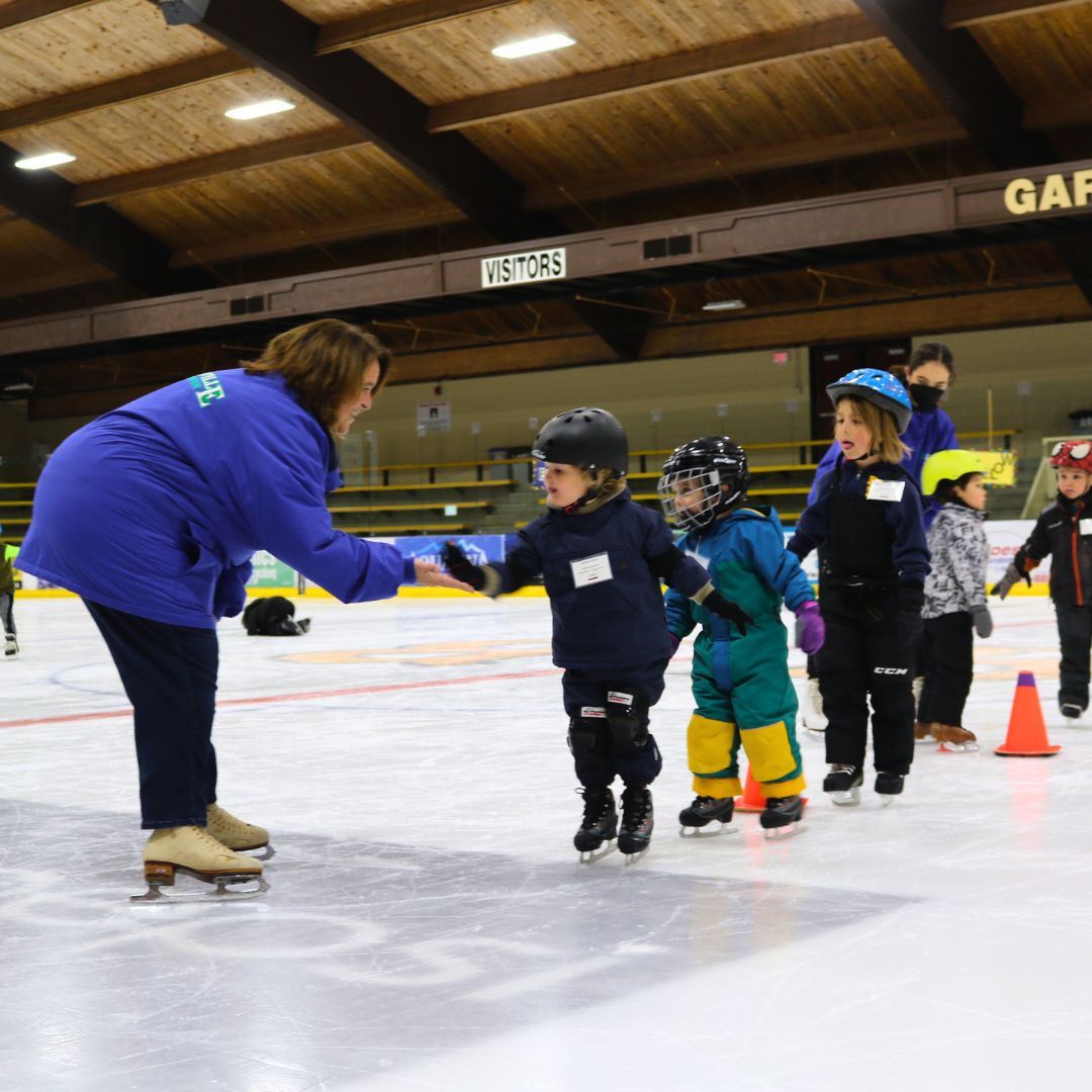 Kids on the ice in a line with an instructor leading