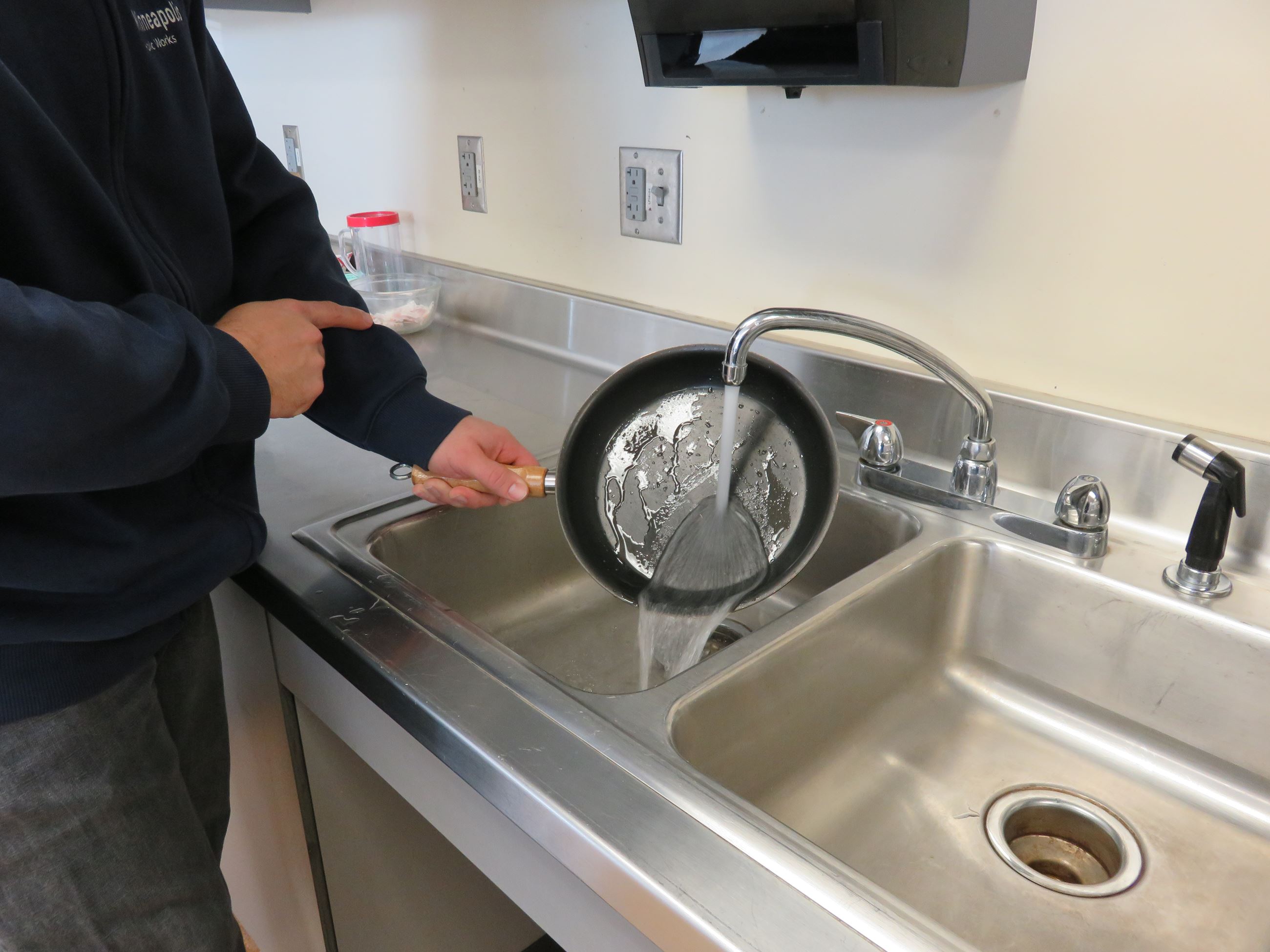 Person rinsing small fry pan with water.