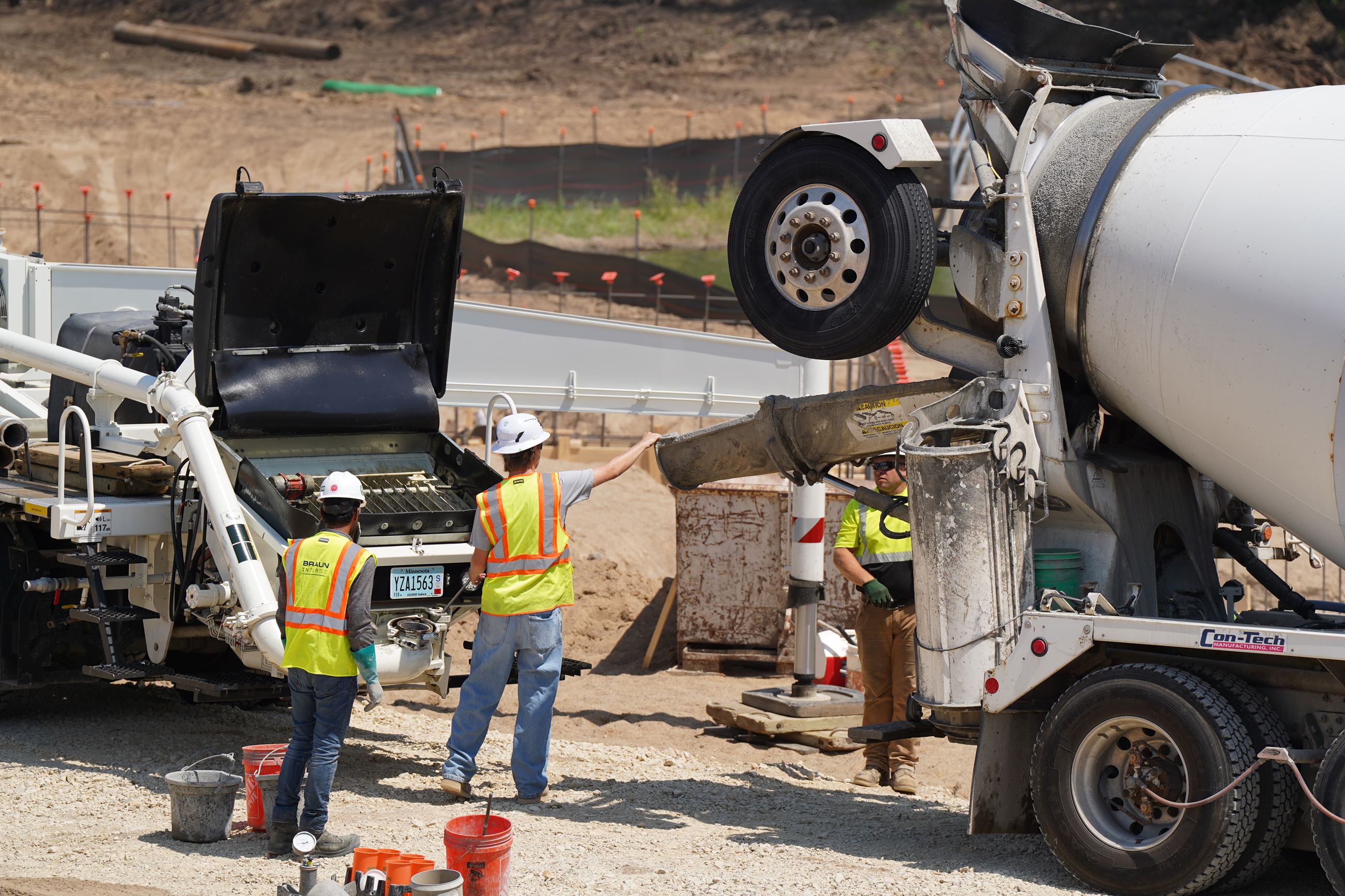 Construction workers guiding concrete truck to pour into pump truck